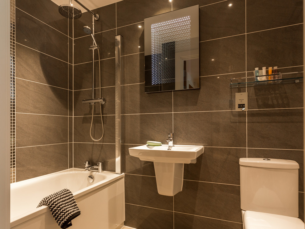 Small contemporary family bathroom in Dorset with a built-in bath, a shower/bath combination, a one-piece toilet, grey tiles, ceramic tiles, grey walls, ceramic flooring and a wall-mounted sink.