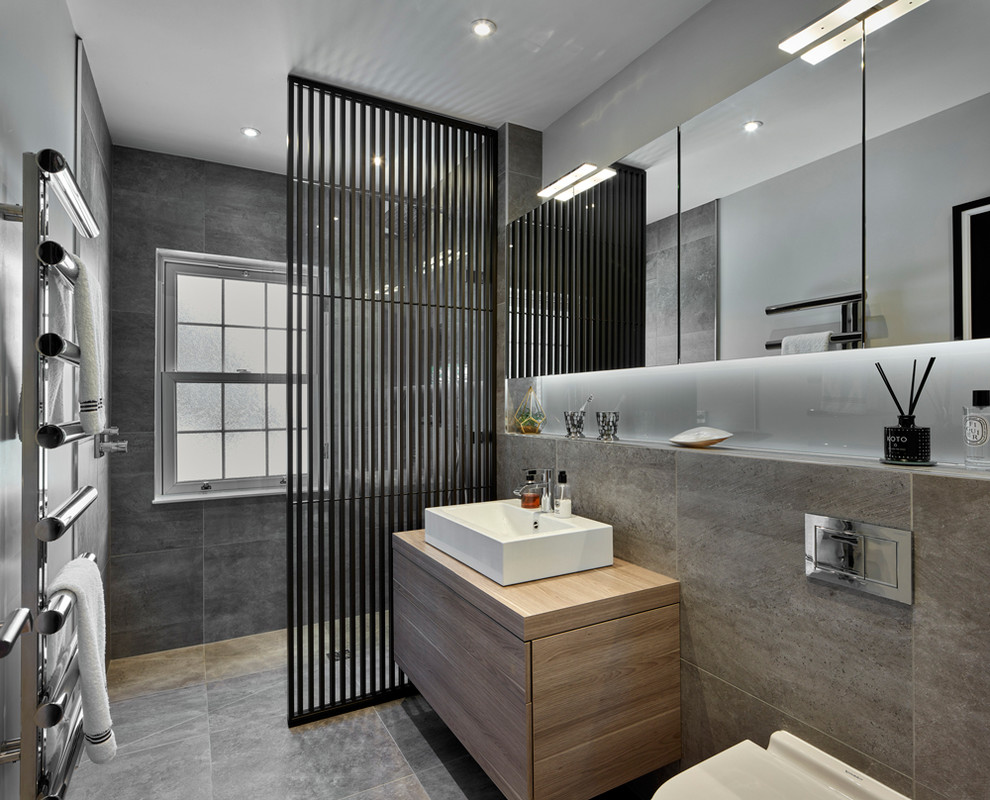 Modern inredning av ett mellanstort badrum med dusch, med släta luckor, skåp i ljust trä, en öppen dusch, en vägghängd toalettstol, grå kakel, porslinskakel, grå väggar, klinkergolv i porslin, ett väggmonterat handfat, grått golv och med dusch som är öppen