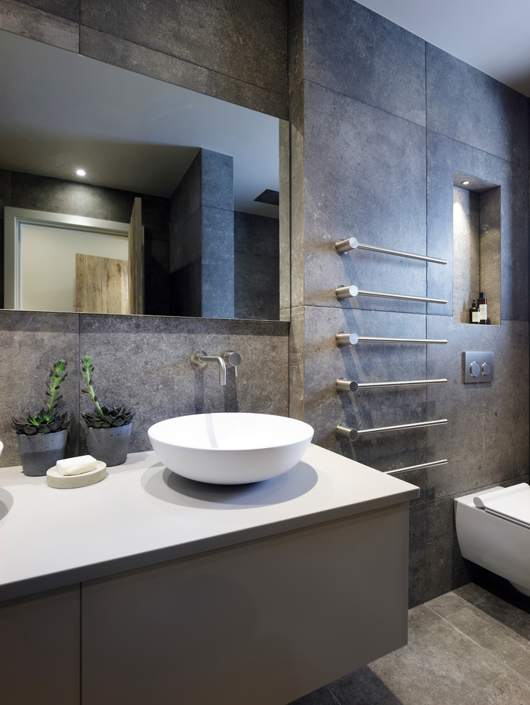 Small trendy master gray tile and ceramic tile ceramic tile and gray floor bathroom photo in Cheshire with flat-panel cabinets, gray cabinets, a wall-mount toilet, gray walls, a trough sink and laminate countertops