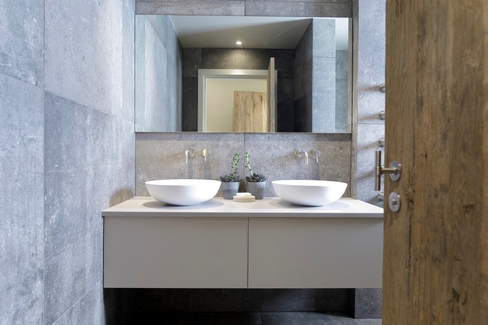 This is an example of a small contemporary ensuite bathroom in Cheshire with flat-panel cabinets, grey cabinets, a walk-in shower, a wall mounted toilet, grey tiles, ceramic tiles, grey walls, ceramic flooring, a trough sink, laminate worktops, grey floors and an open shower.