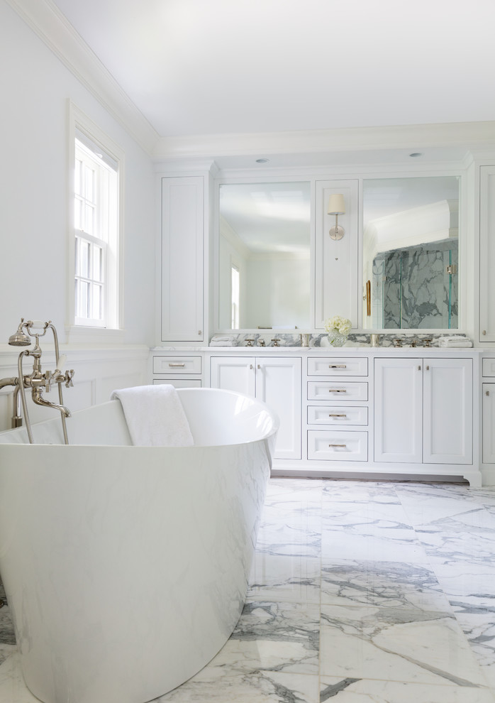 Bild på ett vintage vit vitt en-suite badrum, med vita skåp, marmorgolv, vitt golv, ett fristående badkar, en toalettstol med hel cisternkåpa, vit kakel, marmorkakel, vita väggar, ett undermonterad handfat, marmorbänkskiva och dusch med gångjärnsdörr