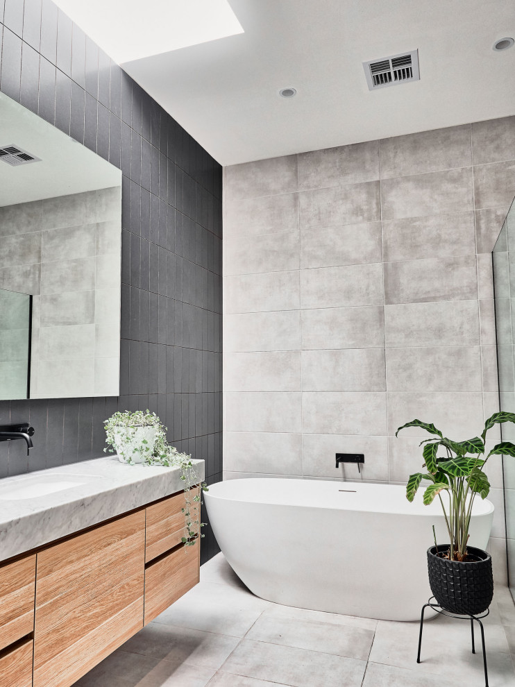 Exempel på ett mellanstort nordiskt grå grått badrum, med möbel-liknande, skåp i ljust trä, ett fristående badkar, svart kakel, grå väggar och grått golv