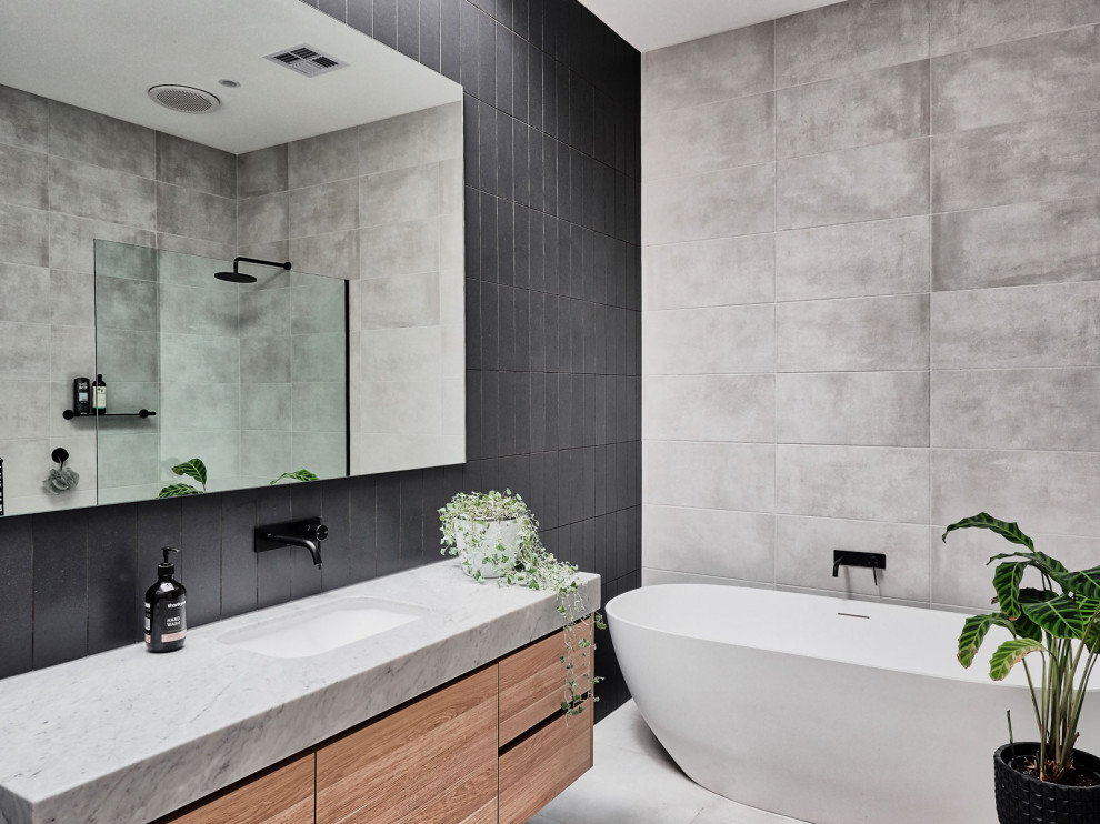 Photo of a medium sized scandinavian bathroom in Melbourne with light wood cabinets, a freestanding bath, a corner shower, black tiles, grey walls, grey floors, an open shower, grey worktops, a single sink, a built in vanity unit and flat-panel cabinets.