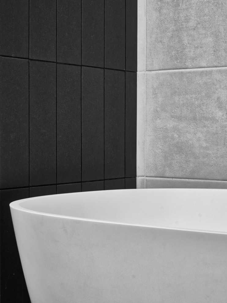 Modelo de cuarto de baño doble y a medida nórdico de tamaño medio con armarios tipo mueble, puertas de armario de madera clara, bañera exenta, ducha esquinera, baldosas y/o azulejos negros, paredes grises, suelo gris, ducha abierta y encimeras grises