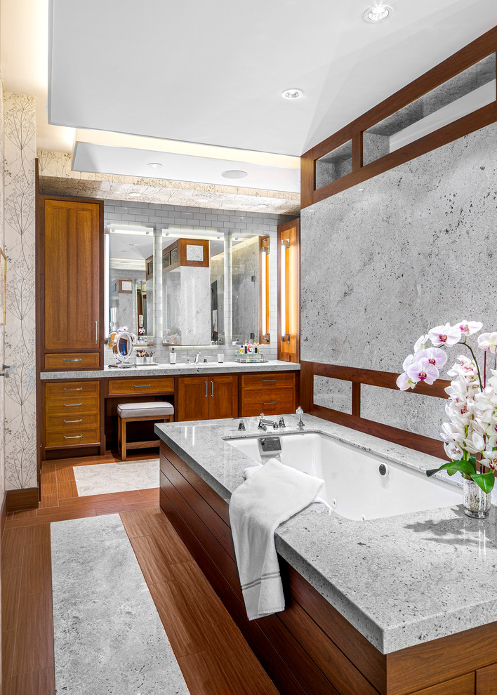 Klassisk inredning av ett mycket stort en-suite badrum, med luckor med infälld panel, skåp i mellenmörkt trä, granitbänkskiva, ett undermonterat badkar, grå kakel, stenhäll och grå väggar