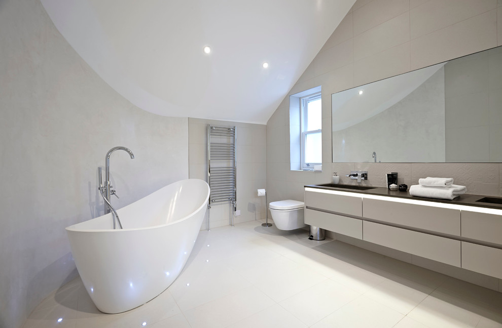 Свежая идея для дизайна: ванная комната в современном стиле с монолитной раковиной, плоскими фасадами, серыми фасадами, отдельно стоящей ванной, инсталляцией, бежевой плиткой и бежевыми стенами - отличное фото интерьера