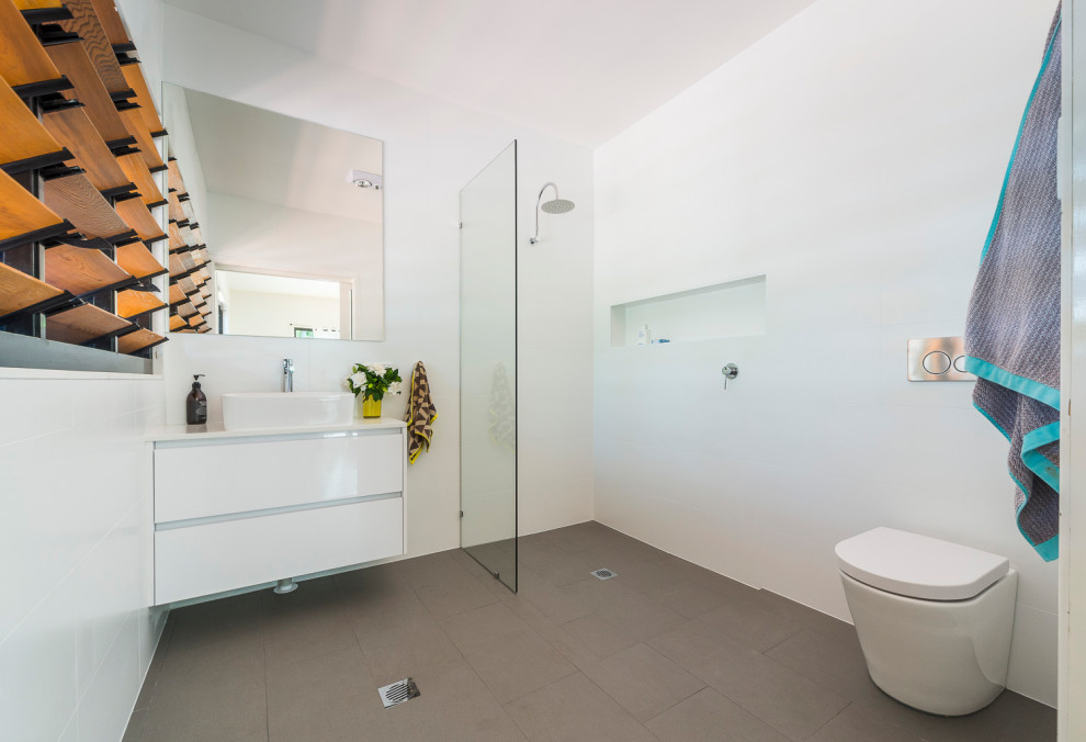 Bild på ett stort funkis vit vitt badrum för barn, med ett fristående badkar, en öppen dusch, en toalettstol med hel cisternkåpa, vit kakel, porslinskakel, vita väggar, klinkergolv i porslin, bänkskiva i kvarts, grått golv och med dusch som är öppen
