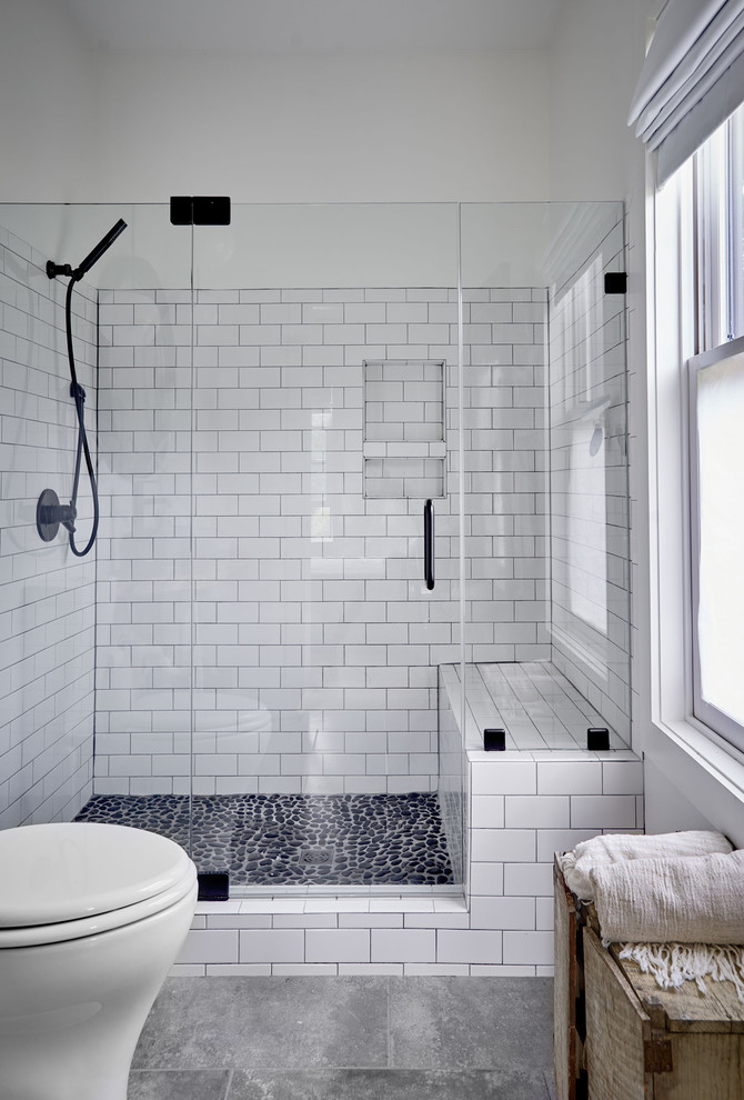 Lantlig inredning av ett mellanstort badrum, med vit kakel, porslinskakel, vita väggar, klinkergolv i småsten, dusch med gångjärnsdörr, en dusch i en alkov och grått golv