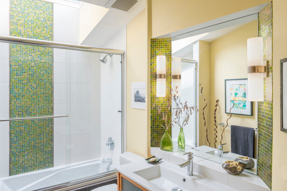 Пример оригинального дизайна: главная ванная комната среднего размера в стиле фьюжн с стеклянными фасадами, фасадами цвета дерева среднего тона, ванной в нише, душем над ванной, желтыми стенами, монолитной раковиной, столешницей из искусственного камня и душем с раздвижными дверями