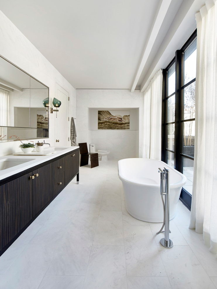 This is an example of a large modern ensuite bathroom in New York with flat-panel cabinets, dark wood cabinets, a freestanding bath, white walls, marble flooring, a built-in sink and granite worktops.