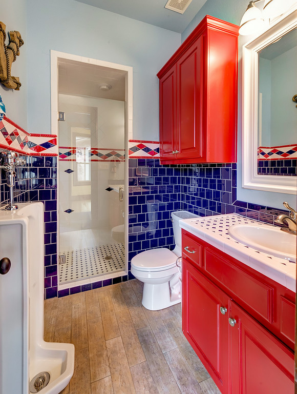 Bild på ett mellanstort vintage flerfärgad flerfärgat badrum för barn, med luckor med upphöjd panel, röda skåp, en dusch i en alkov, ett urinoar, flerfärgad kakel, vit kakel, porslinskakel, flerfärgade väggar, mellanmörkt trägolv, ett nedsänkt handfat, kaklad bänkskiva, brunt golv och dusch med gångjärnsdörr