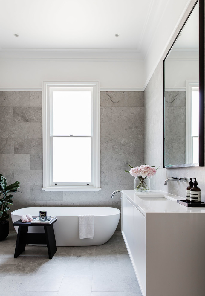 Cette photo montre une salle de bain principale et grise et blanche tendance avec un placard à porte plane, des portes de placard beiges, une baignoire indépendante, un mur beige et un lavabo encastré.