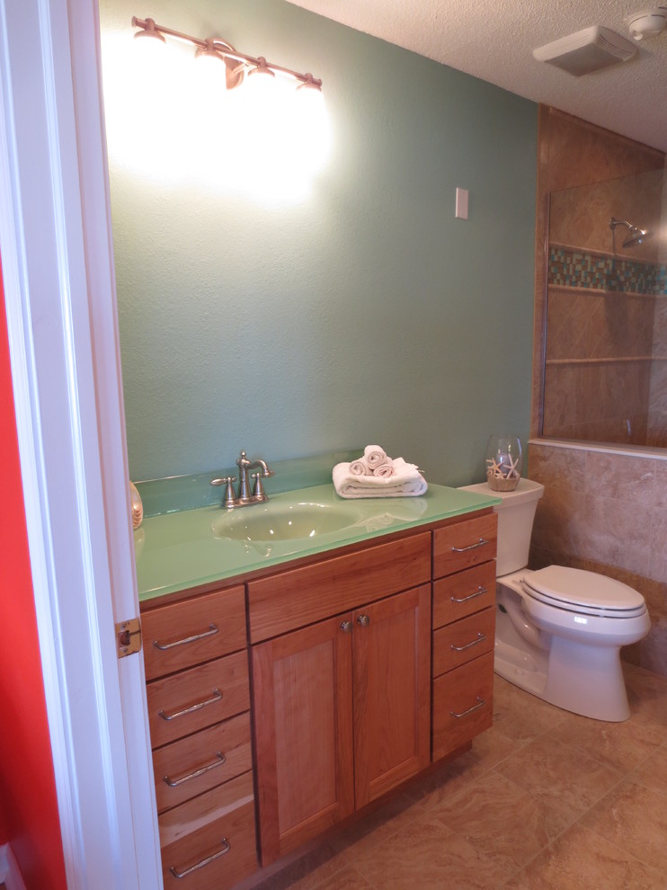 На фото: ванная комната в стиле фьюжн с монолитной раковиной, фасадами в стиле шейкер, фасадами цвета дерева среднего тона, стеклянной столешницей, раздельным унитазом, бежевой плиткой и керамогранитной плиткой