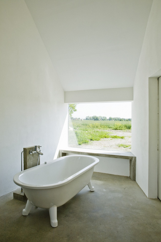 Inredning av ett minimalistiskt badrum, med ett badkar med tassar och betonggolv