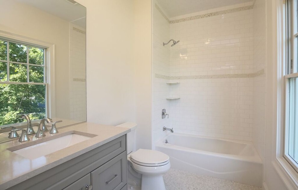 На фото: детская, серо-белая ванная комната среднего размера в стиле неоклассика (современная классика) с ванной в нише, душем над ванной, белыми стенами, серыми фасадами, столешницей из известняка, фасадами с утопленной филенкой, раздельным унитазом, белой плиткой, плиткой кабанчик, полом из мозаичной плитки и врезной раковиной