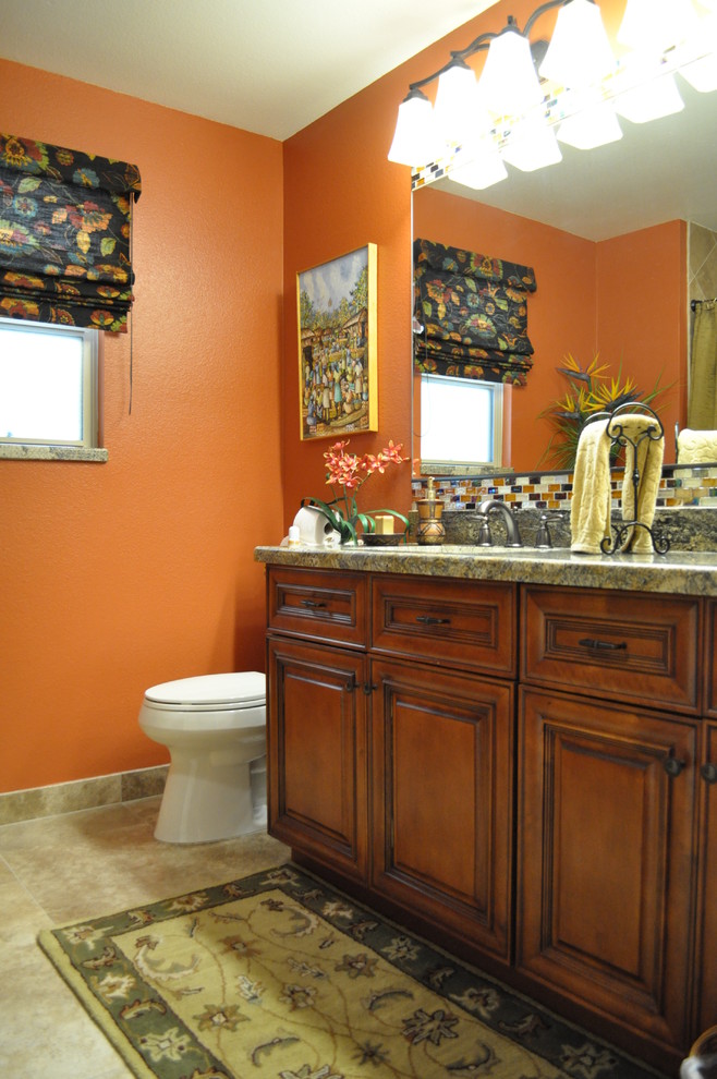 Foto på ett rustikt badrum, med ett undermonterad handfat, skåp i mellenmörkt trä, granitbänkskiva, en toalettstol med hel cisternkåpa, flerfärgad kakel, glasskiva, orange väggar och klinkergolv i porslin
