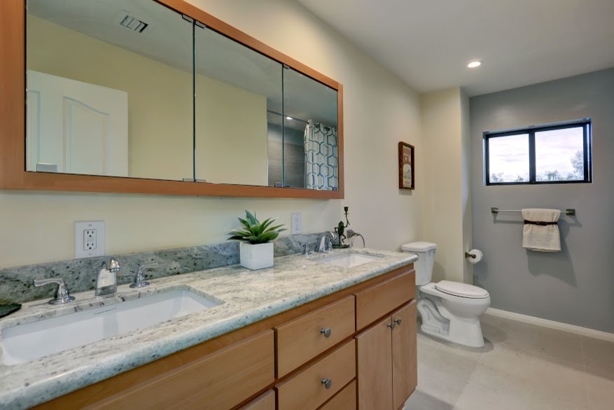 Immagine di una grande stanza da bagno country con lavabo sottopiano, ante lisce, ante in legno chiaro, top in granito, WC monopezzo e piastrelle beige