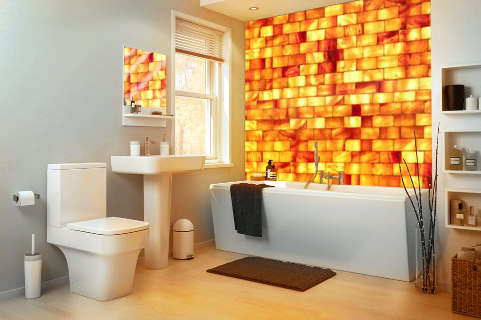 Bild på ett mellanstort funkis badrum, med ett fristående badkar, en toalettstol med separat cisternkåpa, orange kakel, grå väggar, ljust trägolv, ett piedestal handfat och beiget golv