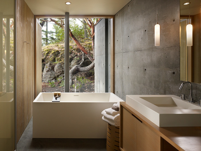 На фото: ванная комната в современном стиле с настольной раковиной, плоскими фасадами, светлыми деревянными фасадами, столешницей из дерева, отдельно стоящей ванной, серыми стенами и бетонным полом с