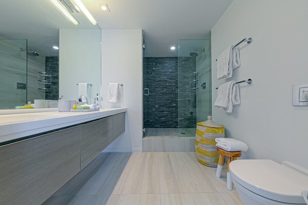 Bild på ett stort funkis badrum med dusch, med släta luckor, grå skåp, en dusch i en alkov, en toalettstol med hel cisternkåpa, grå kakel, stenhäll, vita väggar, ett integrerad handfat och klinkergolv i porslin