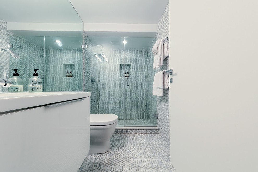 Cette image montre une salle de bain minimaliste de taille moyenne avec un placard à porte plane, des portes de placard blanches, WC à poser, un carrelage gris, un carrelage blanc, mosaïque, un mur gris, un sol en carrelage de terre cuite et un lavabo intégré.
