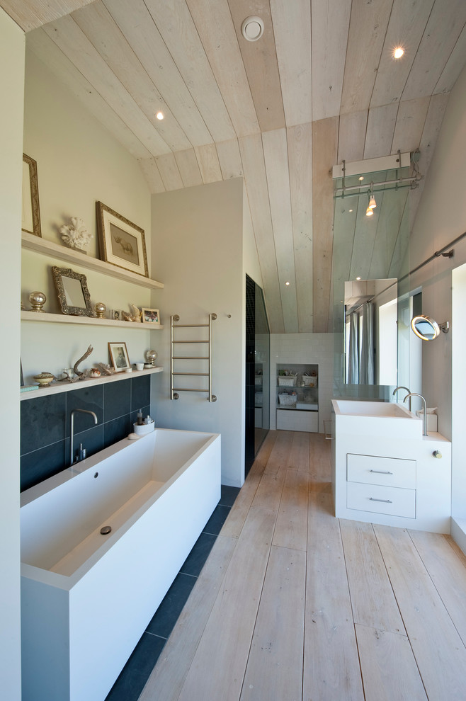Modernes Badezimmer En Suite mit Trogwaschbecken, flächenbündigen Schrankfronten, weißen Schränken, freistehender Badewanne, grauen Fliesen, weißer Wandfarbe und hellem Holzboden in London