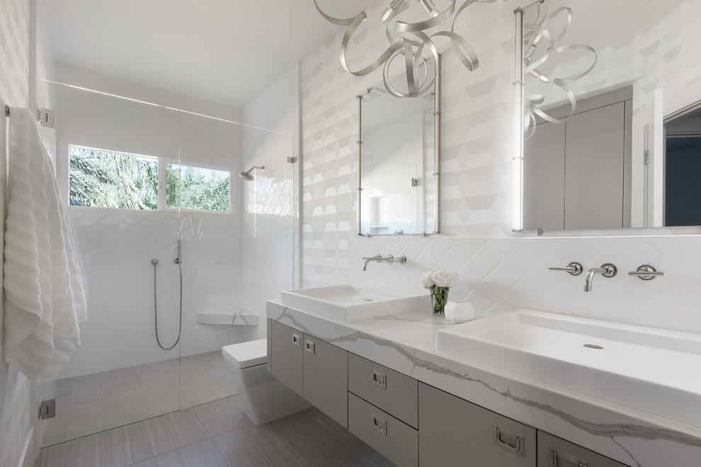 Пример оригинального дизайна: большая главная ванная комната в современном стиле с плоскими фасадами, серыми фасадами, душем без бортиков, белой плиткой, белыми стенами, настольной раковиной, серым полом, душем с распашными дверями, белой столешницей, керамогранитной плиткой, полом из керамогранита, мраморной столешницей, окном и зеркалом с подсветкой