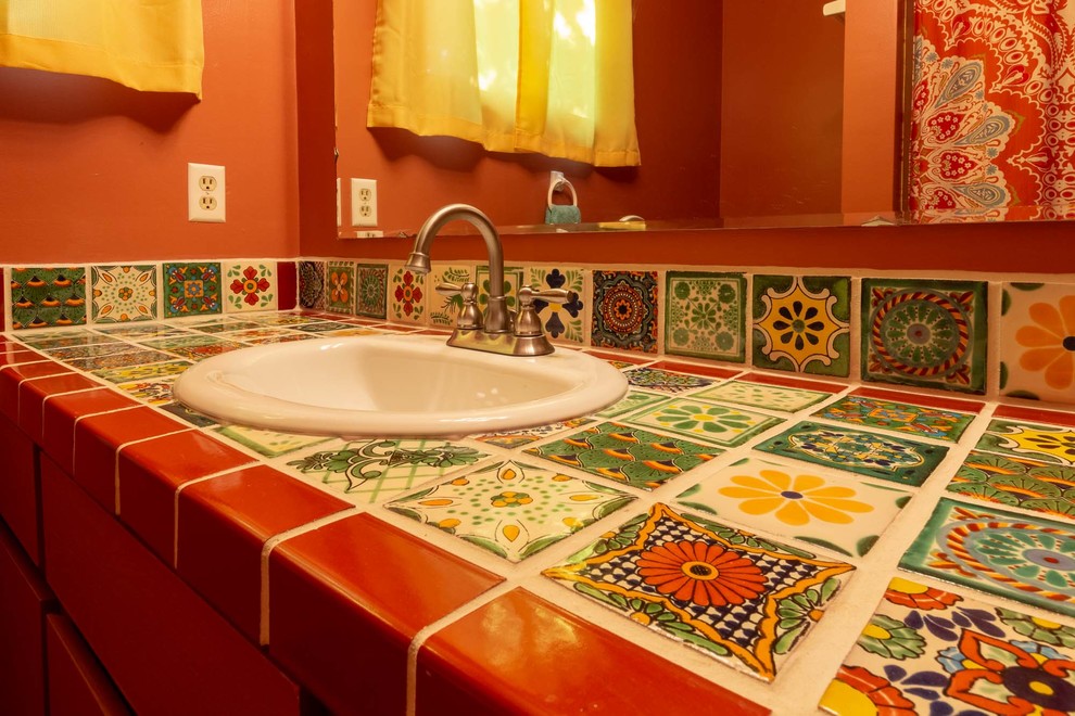 Cette image montre une salle de bain sud-ouest américain de taille moyenne avec un placard à porte plane, des portes de placard marrons, une baignoire en alcôve, un combiné douche/baignoire, WC à poser, un mur marron, un sol en carrelage de céramique, un lavabo posé, un sol vert, une cabine de douche avec un rideau et un plan de toilette multicolore.