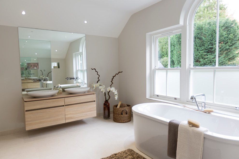 Freestanding bathtub - transitional master freestanding bathtub idea in Surrey with a vessel sink, flat-panel cabinets, light wood cabinets, wood countertops, gray walls and beige countertops