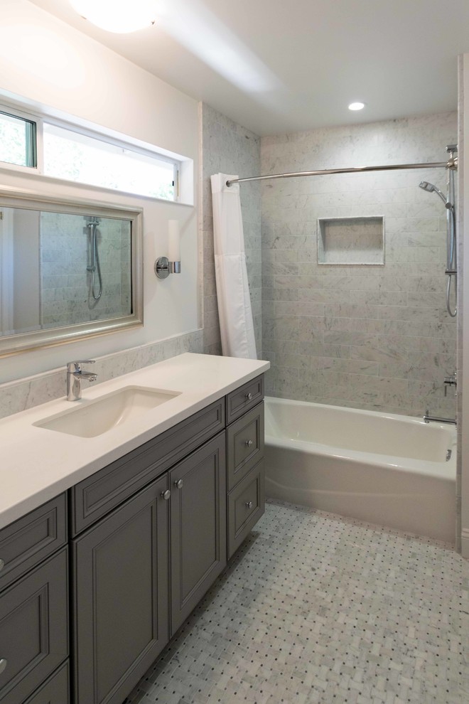Aménagement d'une salle de bain contemporaine de taille moyenne avec un placard avec porte à panneau surélevé, des portes de placard grises, une baignoire posée, un combiné douche/baignoire, un carrelage gris, un carrelage métro, un mur blanc, un sol en marbre, un lavabo encastré et un plan de toilette en marbre.