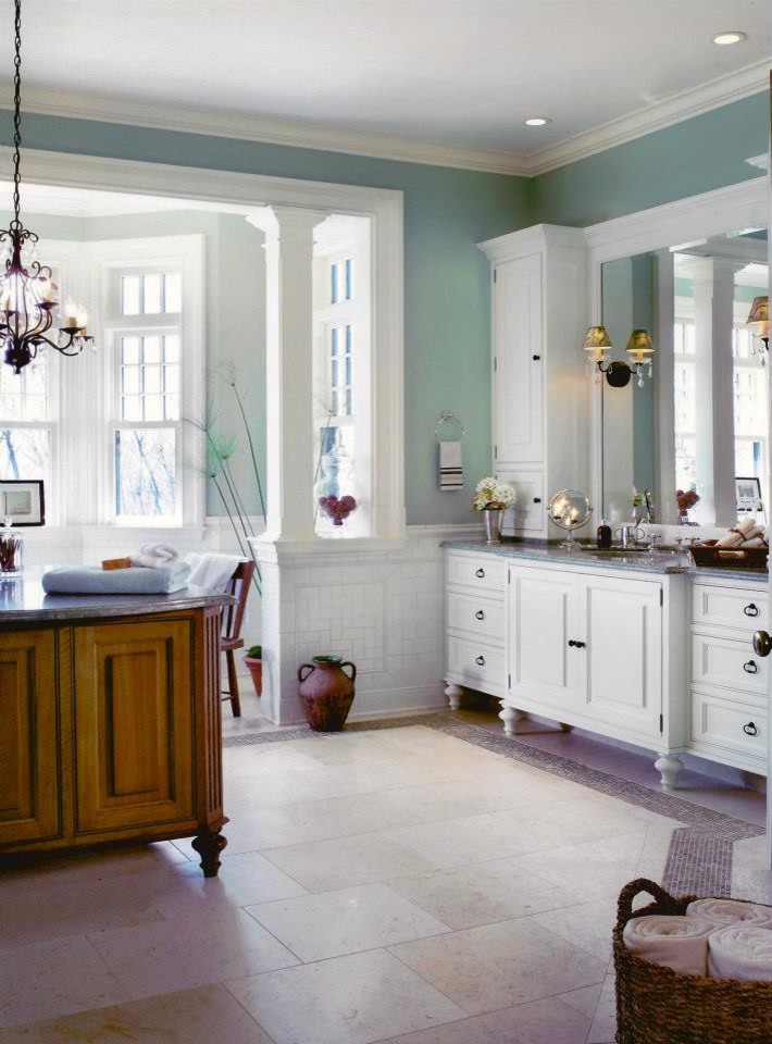 Klassisk inredning av ett stort badrum, med ett undermonterad handfat, luckor med profilerade fronter, vita skåp, granitbänkskiva, ett fristående badkar, en toalettstol med separat cisternkåpa, beige kakel, gröna väggar och kalkstensgolv