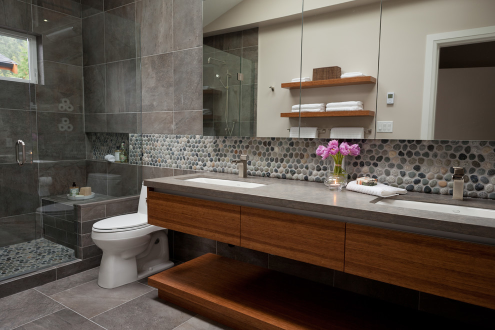 Ejemplo de cuarto de baño contemporáneo con encimera de piedra caliza, lavabo bajoencimera, puertas de armario de madera en tonos medios y suelo de baldosas tipo guijarro