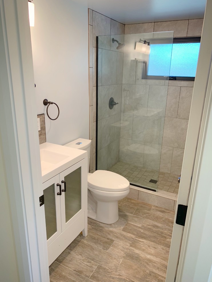 Modern inredning av ett litet vit vitt badrum med dusch, med luckor med glaspanel, vita skåp, en dusch i en alkov, vit kakel, stenhäll, ljust trägolv, ett integrerad handfat, bänkskiva i akrylsten och med dusch som är öppen