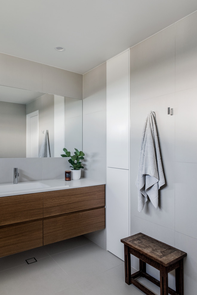 Imagen de cuarto de baño contemporáneo con armarios con paneles lisos, puertas de armario de madera en tonos medios, paredes grises, lavabo integrado y suelo gris