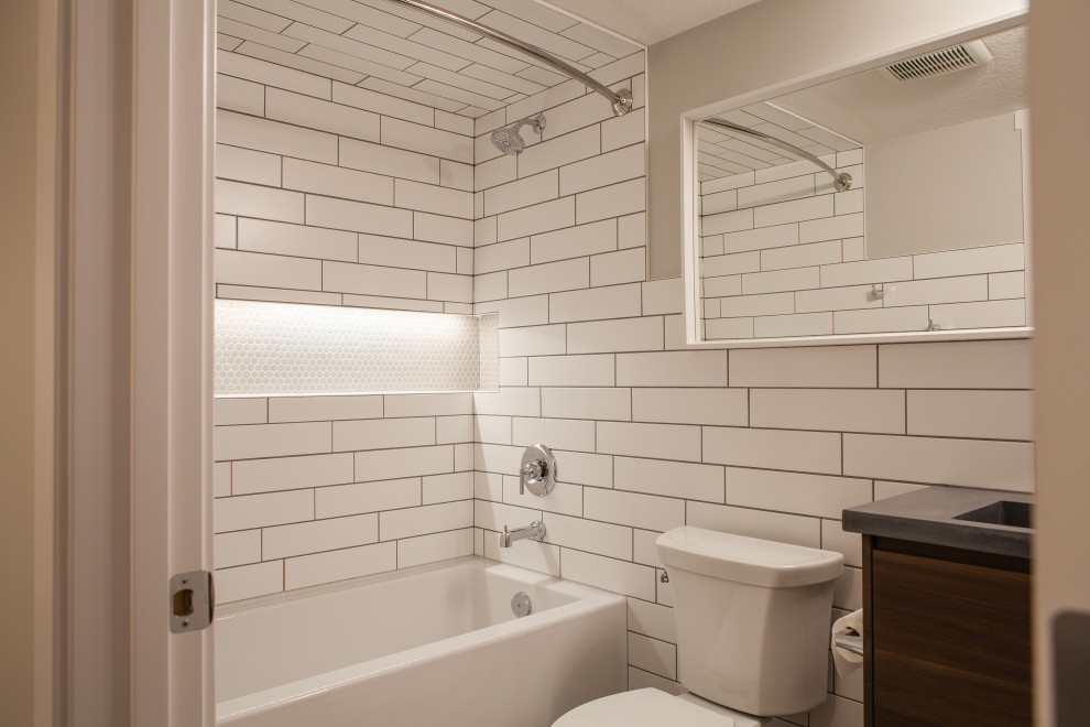 Photo of a medium sized contemporary ensuite bathroom in Calgary with flat-panel cabinets, brown cabinets, an alcove bath, a shower/bath combination, a two-piece toilet, white tiles, ceramic tiles, grey walls, vinyl flooring, an integrated sink, concrete worktops, grey floors, a shower curtain and grey worktops.