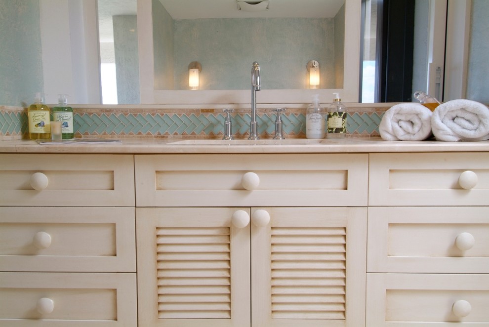 Inredning av ett maritimt badrum, med ett undermonterad handfat, luckor med lamellpanel, beige skåp, marmorbänkskiva, beige kakel och stenkakel