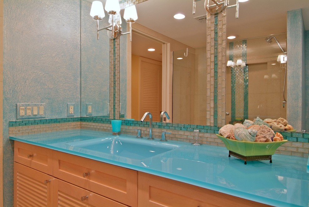Идея дизайна: ванная комната в морском стиле с монолитной раковиной, фасадами с филенкой типа жалюзи, фасадами цвета дерева среднего тона, стеклянной столешницей, синей плиткой и синей столешницей