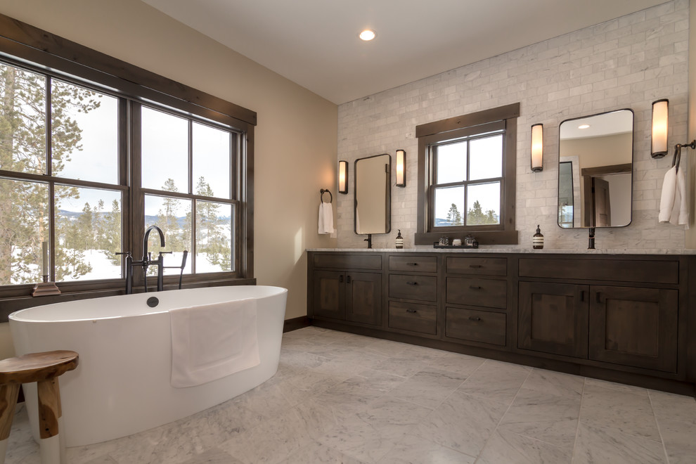 Design ideas for a large rustic ensuite bathroom in Denver with shaker cabinets, dark wood cabinets, a freestanding bath, grey tiles, stone tiles, beige walls, a submerged sink, granite worktops, grey floors and grey worktops.