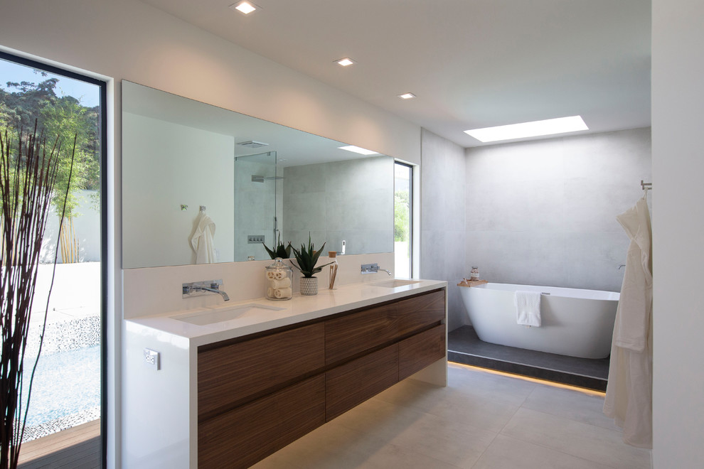 Modernes Badezimmer mit flächenbündigen Schrankfronten, hellbraunen Holzschränken, freistehender Badewanne, grauen Fliesen, weißer Wandfarbe, Unterbauwaschbecken, grauem Boden und weißer Waschtischplatte in San Diego