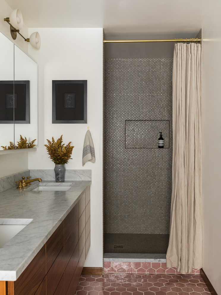 Inredning av ett 60 tals grå grått badrum, med släta luckor, skåp i mellenmörkt trä, en dusch i en alkov, grå kakel, mosaik, vita väggar, ett undermonterad handfat, brunt golv och dusch med duschdraperi