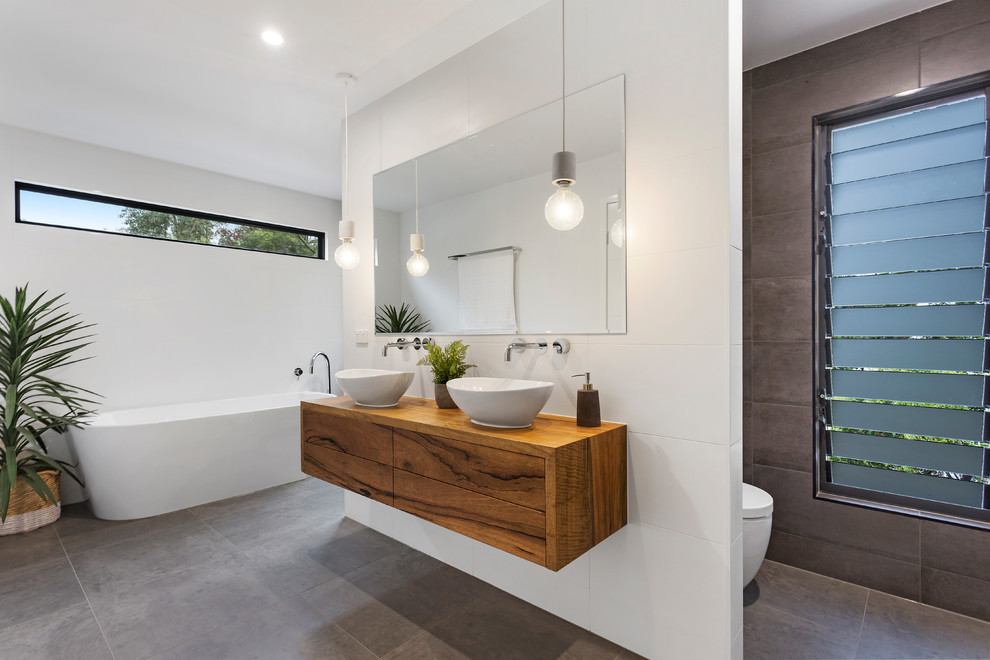 Maritimes Badezimmer mit hellbraunen Holzschränken, freistehender Badewanne, Porzellanfliesen, grauer Wandfarbe und grauem Boden in Sunshine Coast