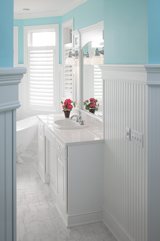 Cette photo montre une grande salle de bain principale chic avec un placard avec porte à panneau surélevé, des portes de placard blanches, une baignoire indépendante, un mur bleu, un sol en marbre, un lavabo posé et un plan de toilette en marbre.