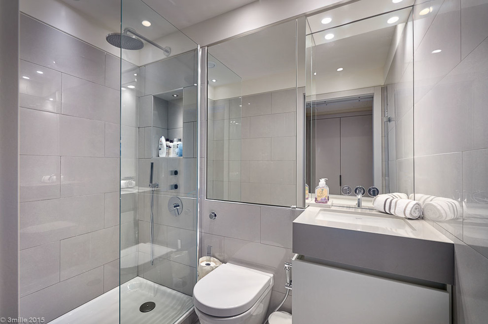 Imagen de cuarto de baño moderno pequeño con ducha esquinera, sanitario de pared, baldosas y/o azulejos grises, paredes grises, aseo y ducha y lavabo bajoencimera