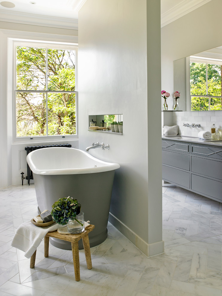 Inspiration for a large transitional master white tile and stone tile marble floor freestanding bathtub remodel in London with gray cabinets, gray walls and flat-panel cabinets