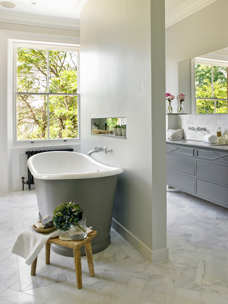 Large traditional ensuite bathroom in London with grey cabinets, a freestanding bath, white tiles, grey walls, stone tiles, marble flooring and flat-panel cabinets.