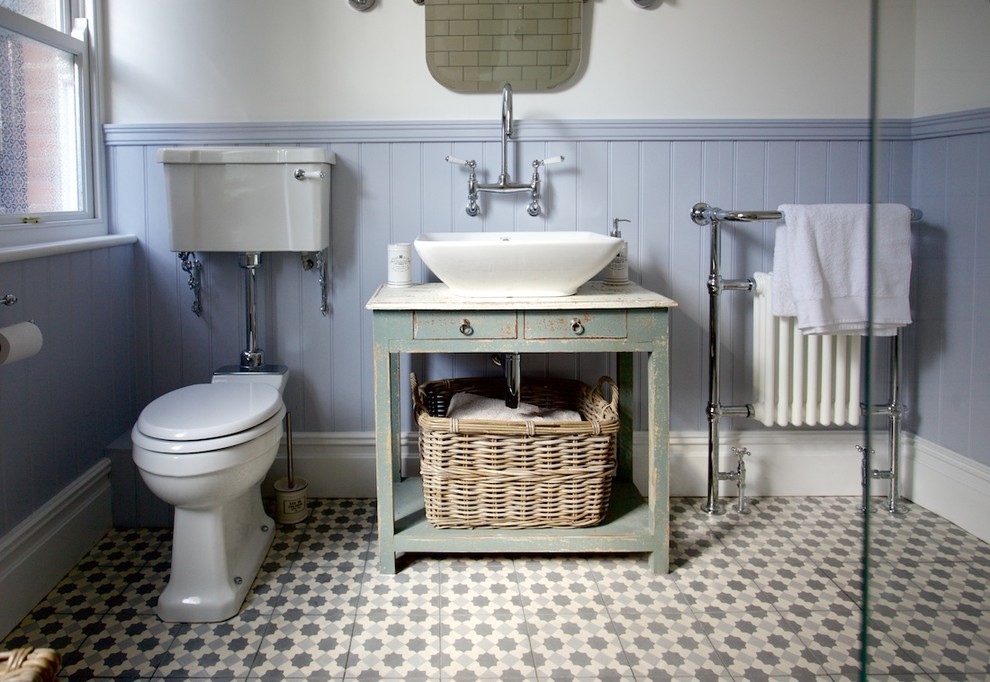 Photo of a medium sized classic bathroom in Sussex with a console sink, freestanding cabinets, distressed cabinets, a claw-foot bath, a shower/bath combination, a two-piece toilet, multi-coloured tiles, cement tiles and beige walls.