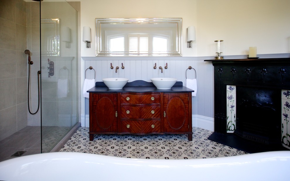 Large classic ensuite bathroom in Sussex with a vessel sink, freestanding cabinets, medium wood cabinets, granite worktops, a freestanding bath, a corner shower, a two-piece toilet, multi-coloured tiles, ceramic tiles, beige walls and ceramic flooring.