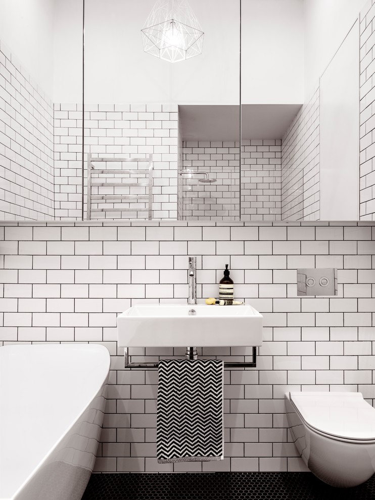 Bild på ett litet funkis badrum, med ett fristående badkar, en dusch i en alkov, en vägghängd toalettstol, vit kakel, tunnelbanekakel, vita väggar, mosaikgolv, ett väggmonterat handfat, luckor med glaspanel, bänkskiva i koppar, svart golv och dusch med gångjärnsdörr