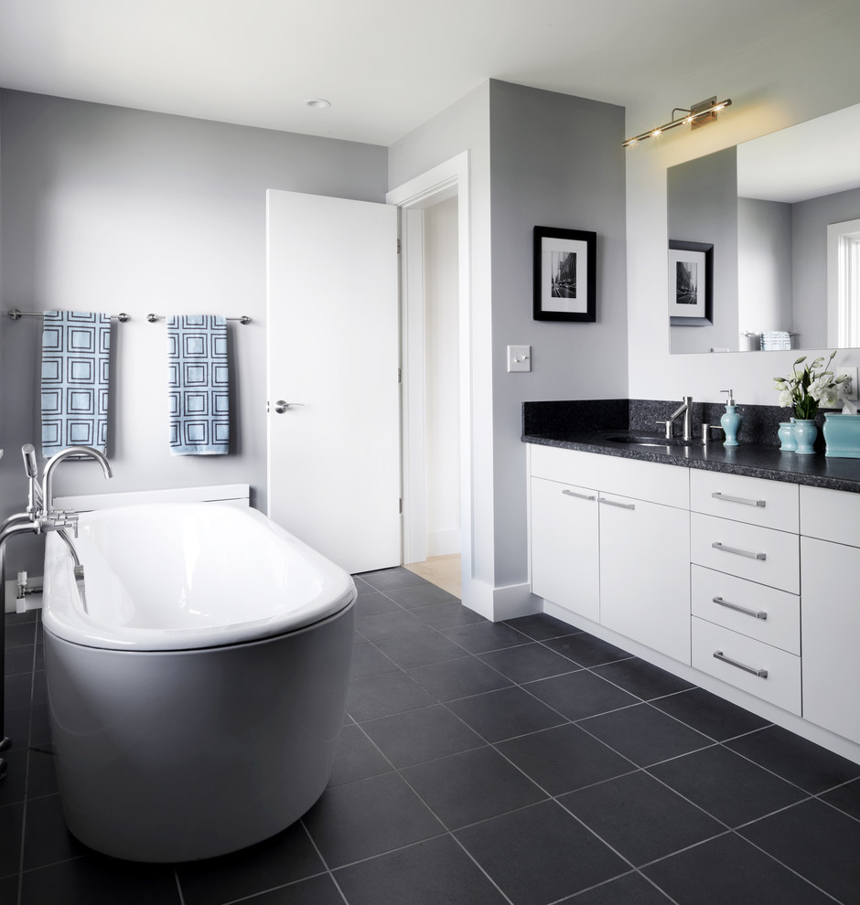 Cette image montre une salle de bain grise et blanche design avec une baignoire indépendante, un sol noir et un plan de toilette noir.
