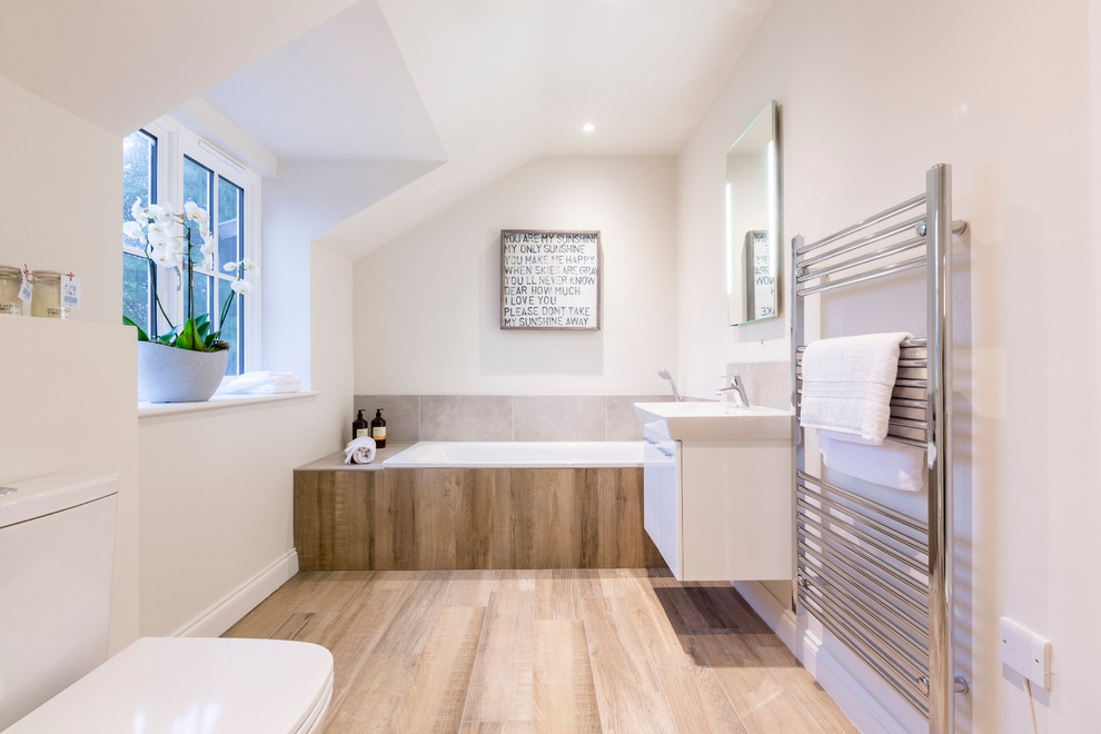Modernes Badezimmer mit flächenbündigen Schrankfronten, weißen Schränken, Badewanne in Nische, braunen Fliesen, weißer Wandfarbe, Waschtischkonsole und Wandtoilette mit Spülkasten in London
